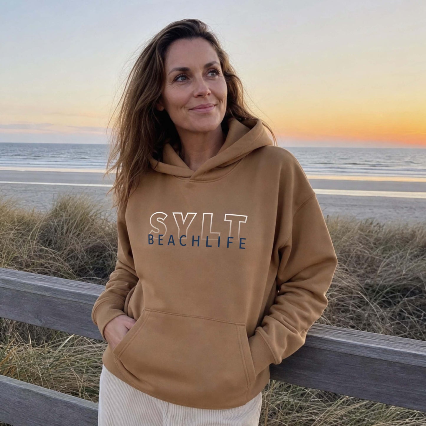 Frau steht auf Sylt am Strand mit einem reed farbigen BEACHLIFE SYLT Gradient Hoodie